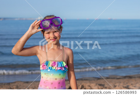 Child girl smiling on beach in colorful swimsuit and purple diving goggles Child girl smiling on beach in colorful swimsuit and purple diving goggles 126586993