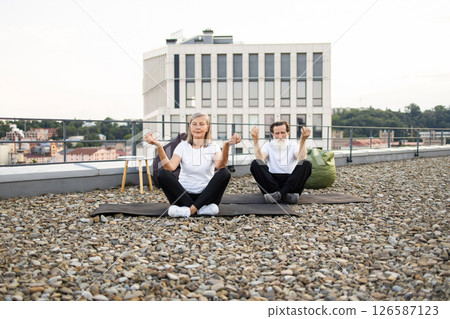 Two elderly individuals, female and male, sitting in lotus pose during yoga session outdoors on rooftop urban area emphasizing wellness, relaxation, and fitness 126587123