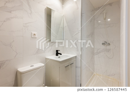 Compact bathroom with marble wall tiles white sink black faucet and shower enclosure with glass wall 126587445
