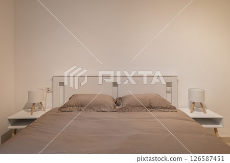 Front view of bedroom with taupe bedding, white bedframe and matching nightstands and lamps Front view of bedroom with taupe bedding, white bedframe and matching nightstands and lamps 126587451