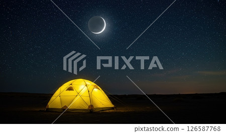 Camping under a starry sky with a crescent moon illuminating the yellow tent 126587768