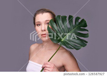 Young caucasian female with monstera leaf posing against neutral background Young caucasian female with monstera leaf posing against neutral background 126587927