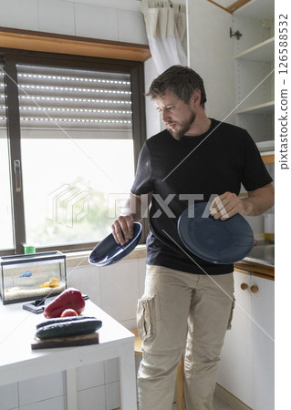 Man preparing lunch in kitchen holding plates near fish tank and vegetables Man preparing lunch in kitchen holding plates near fish tank and vegetables 126588532