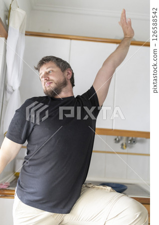 Man stretching arm and leg in kitchen 126588542