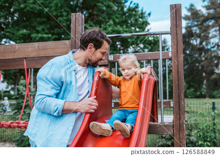 Toddler on a slide with dad's support. Toddler on a slide with dad's support. 126588849