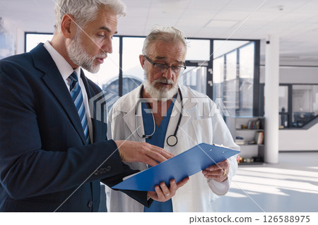 Doctor talking with hospital manager, showing him document in clipboard. 126588975