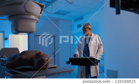 Male patient undergoing X-ray examination using tilting radiographic wall stand. 126589015