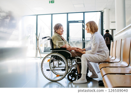 Elderly patient in wheelchair talking with female physician. Elderly patient in wheelchair talking with female physician. 126589040