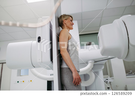 Female patient undergoing dynamic X-ray scan using tilting fluoroscopy wall unit. 126589209