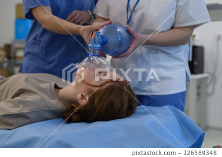 Medical staff applying oxygen mask to unconscious teenage girl in hospital. 126589348