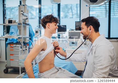 Teen boy undergoing medical checkup with doctor in hospital room. 126589444