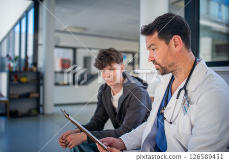 Doctor explaining medical procedure to teenage patient in hospital waiting room. Doctor explaining medical procedure to teenage patient in hospital waiting room. 126589451