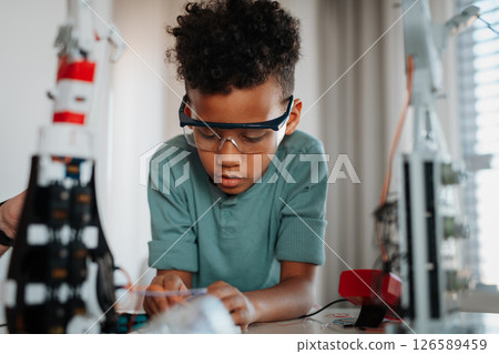 Focused boy working on small robot toy at home. 126589459