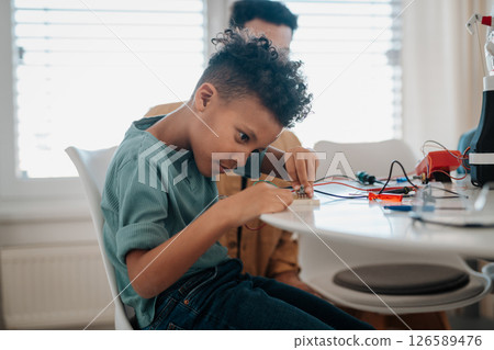 Young schoolboy assembling robotic kit, working with circuit board at home. 126589476