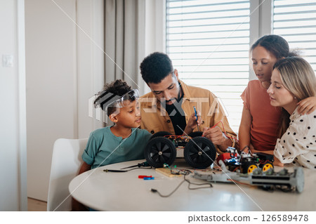 Parents building toy robotic kit with their kids. Robotic car assembling. Parents building toy robotic kit with their kids. Robotic car assembling. 126589478