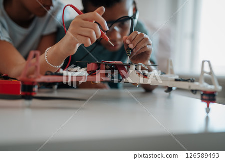 Classmates assembling robotic kit, working with circuit board at home. 126589493