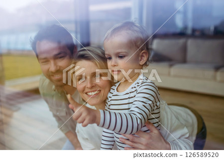 Parents looking out of window with little son, lying on floor. 126589520