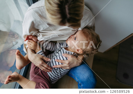 Mother breastfeeding her toddler son by the window 126589526