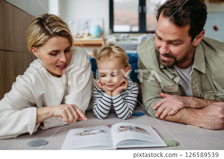 Parents reading book with little son, sitting on floor. 126589539