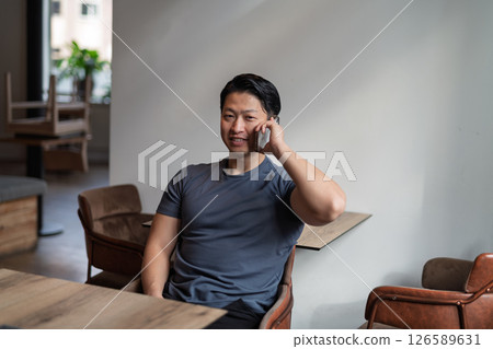 Young asian man talking on phone, sitting at empty table. 126589631