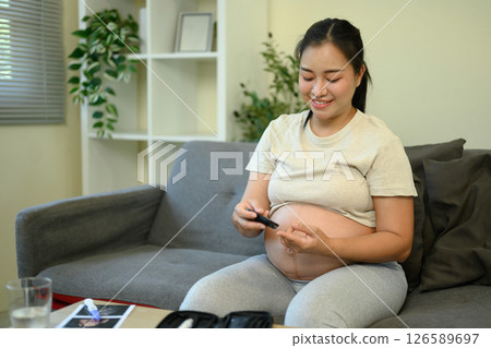 Pregnant woman taking a blood sugar test in a living room 126589697
