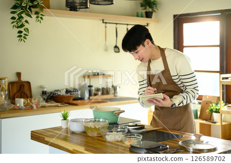 Asian man checking or jotting down a recipe during cooking Asian man checking or jotting down a recipe during cooking 126589702