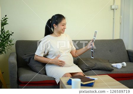 Happy pregnant woman holding her belly and looking at ultrasound photos 126589719