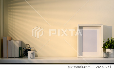 Minimalist workspace with empty frame, plants, books, and accessories in soft morning light Minimalist workspace with empty frame, plants, books, and accessories in soft morning light 126589731