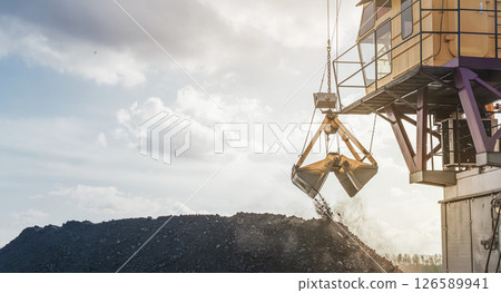 Crane loading coal at port near river under cloudy sky at dusk. Loading coal onto a barge using a floating crane 126589941