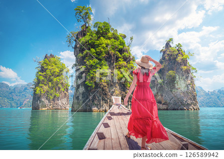 Famous tourist destinations view Thai - Woman solo traveler in red dress on Traditional Thai Longtail boat admiring a famous travel spot Thailand Three Rocks on Cheo Lan Lake in Khaosok Park in Surat 126589942