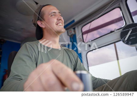 Crane operator actively engaging with joystick in an excavator cab during a sunny workday in the construction site 126589947