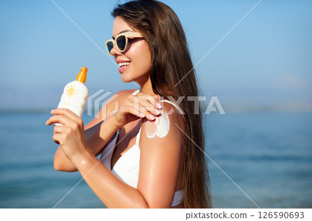 Beautiful Woman in Bikini Applying Sun Cream on Tanned Shoulder. Sun Protection. Skin and Body Care. Girl Using Sunscreen.  Portrait Of Female Holding Suntan Lotion or Moisturizing Sunblock. 126590693