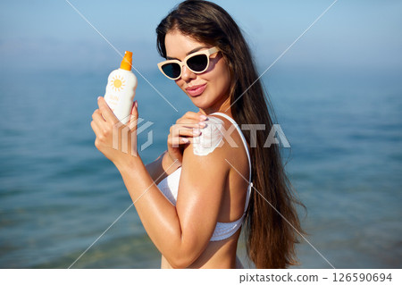 Beautiful Woman in Bikini Applying Sun Cream on Tanned Shoulder. Sun Protection. Skin and Body Care. Girl Using Sunscreen. Portrait Of Female Holding Suntan Lotion or Moisturizing Sunblock. Beautiful Woman in Bikini Applying Sun Cream on Tanned Shoulder. Sun Protection. Skin and Body Care. Girl Using Sunscreen. Portrait Of Female Holding Suntan Lotion or Moisturizing Sunblock. 126590694