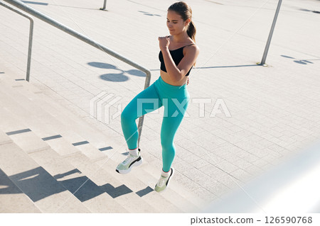 A young athletic woman with a fit body is seen confidently ascending outdoor stairs. Girl wears fitted workout clothes, demonstrating her commitment to a healthy lifestyle. 126590768