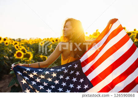 Woman proudly hold waving american USA flag in in the sunflower field. Independence Day, 4th July. Woman proudly hold waving american USA flag in in the sunflower field. Independence Day, 4th July. 126590868