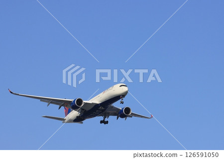 A passenger plane landing against the backdrop of a blue sky. A DELTA plane on approach. 126591050