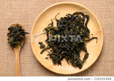 Dried green tea leaves on wooden plate and spoon, Table top view Dried green tea leaves on wooden plate and spoon, Table top view 126591498