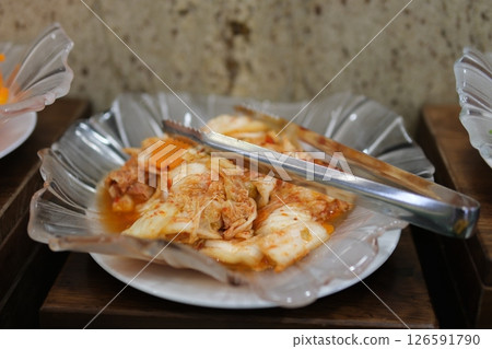Putting homemade kimchi, Korean heritage dish, into a small bowl with wooden serving tongs. 126591790