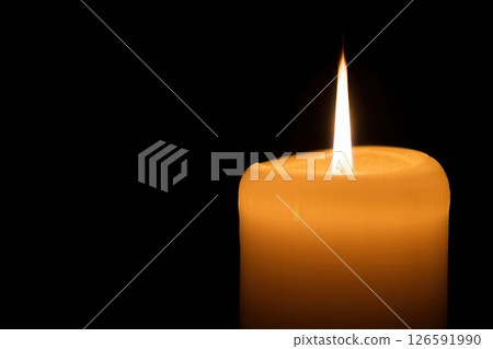 A soft orange glow emanates from a solitary candle casting gentle light in a darkened space. The flame dances gracefully creating an atmosphere of peace and serenity. 126591990