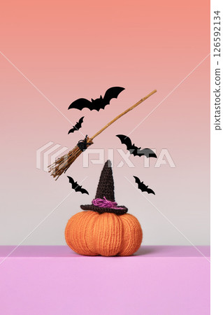 Halloween card made of knitted orange pumpkin with a witch's hat, a broom flying in the air and bats on an orange background and a purple table. Halloween concept. 126592134