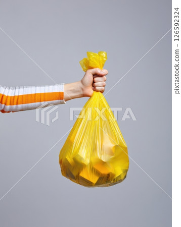 A person grips a yellow trash bag tightly showcasing their commitment to keeping the environment clean and highlighting the importance of waste management practices. 126592324