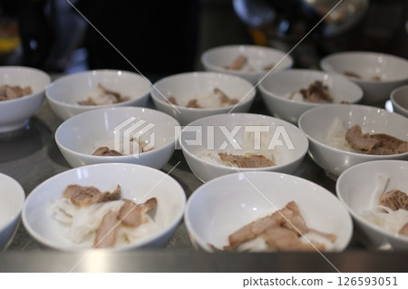 many white soup bowls in buffet rice noodles and pieces of meat waiting to be poured with broth many white soup bowls in buffet rice noodles and pieces of meat waiting to be poured with broth 126593051