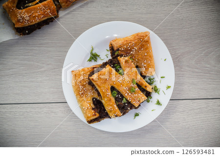 Golden puff pastries with mushroom filling and sesame seeds, on a light wooden table Golden puff pastries with mushroom filling and sesame seeds, on a light wooden table 126593481