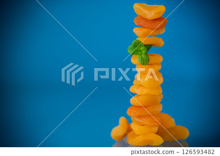 A handful of bright orange dried apricots with a sprig of mint on a blue background A handful of bright orange dried apricots with a sprig of mint on a blue background 126593482