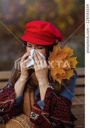 trendy female blowing nose while sitting on bench in city park 126593834