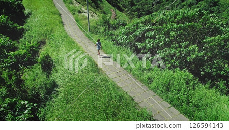 Aerial drone footage of a young woman walking on the Campuhan Ridge Walk in Ubud, Bali, surrounded by lush green vegetation and enjoying the sunny weather 126594143