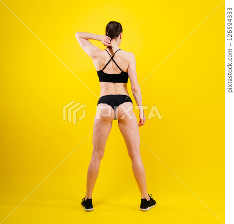 Fit sportswoman in leggings and sports bra looking away and while standing on yellow red 126594333