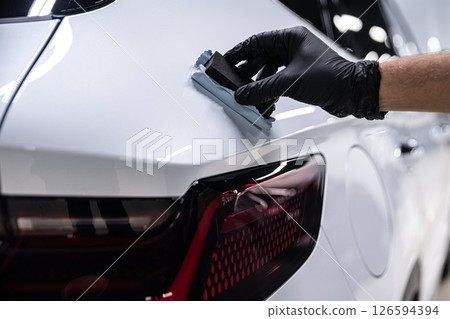 Close-up of a detailer applying ceramic coating to a white car near the rear light. Close-up of a detailer applying ceramic coating to a white car near the rear light. 126594394