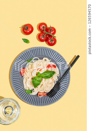 Creamy spaghetti with tomatoes, cheese and basil on a plate on a yellow background 126594570