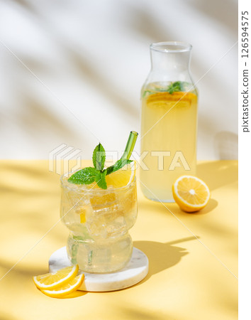 Fresh citrus mojito with lemon, mint and ice on a white yellow background with bottle and shadow. Fresh citrus mojito with lemon, mint and ice on a white yellow background with bottle and shadow. 126594575
